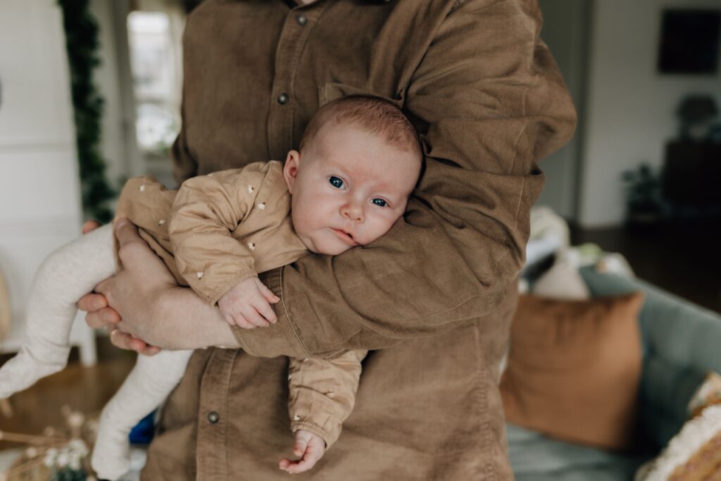 vater haelt sein baby auf dem arm bei neugeborenenshooting