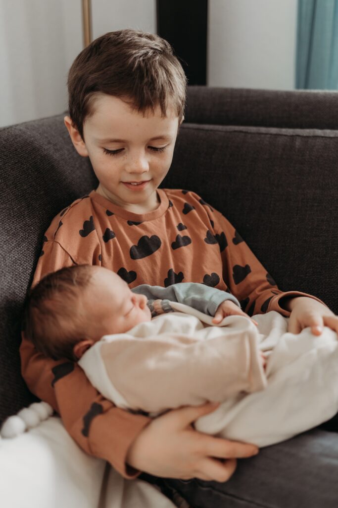 grosser bruder hält baby ins einem arm und schaut es an während eines fotoshootings