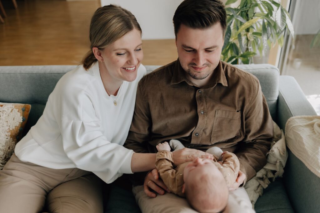 junge eltern sitzen mit baby auf dem sofa und sehen das baby gluecklich an