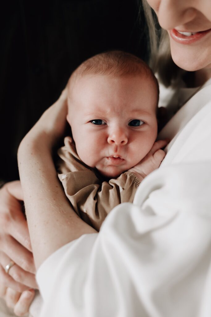 baby liegt auf mamas arm und schaut in die kamera