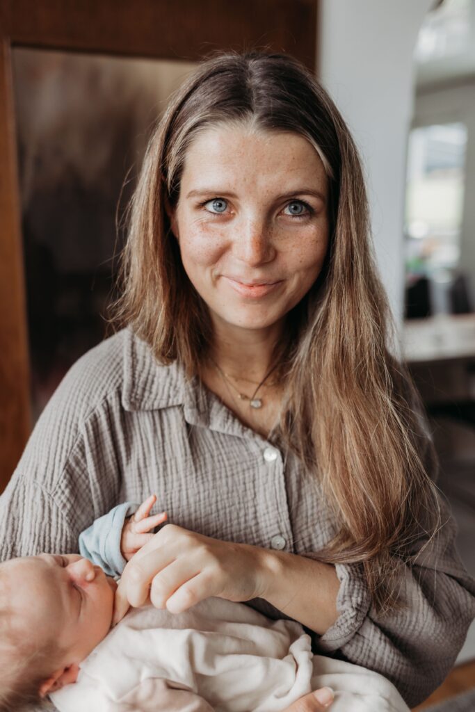 mama schaut gluecklich in die kamera und haelt ihr baby auf dem arm beim neugeborenenshooting in sinsheim